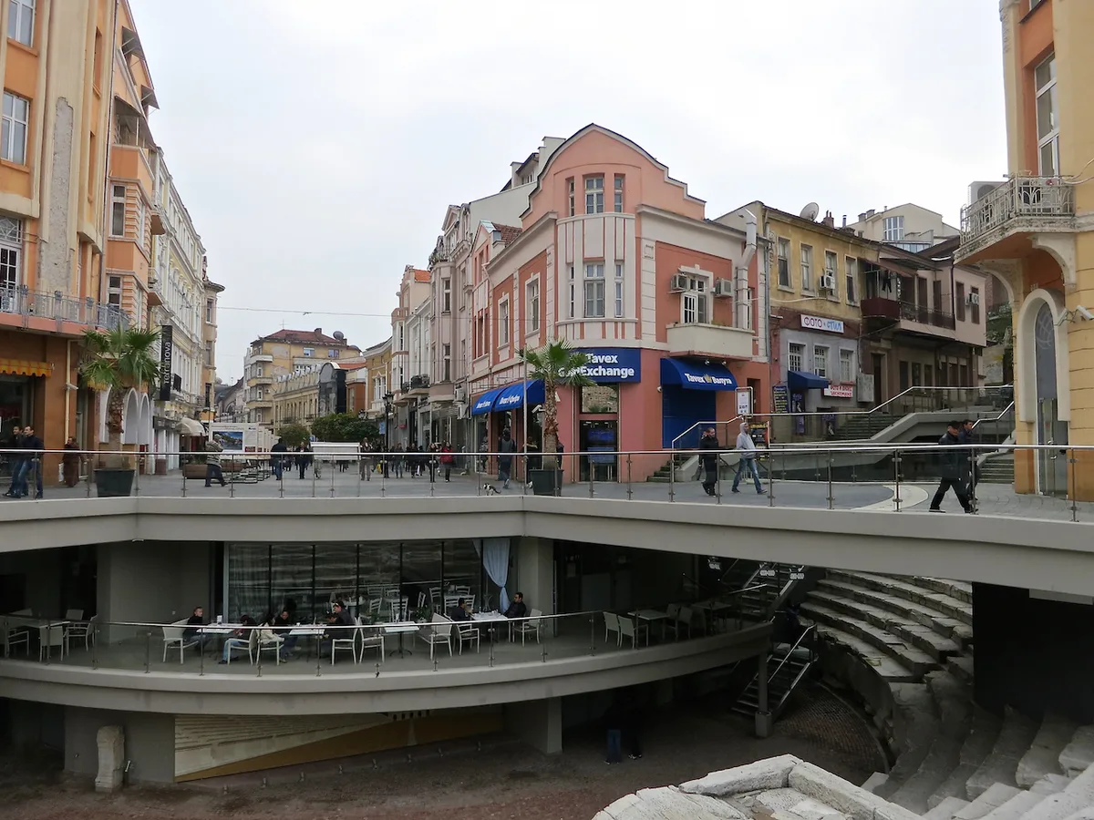 A cafe terrace on the main pedestrian street in Plovdiv, people sitting at tables beside the sunken ancient Roman stadium