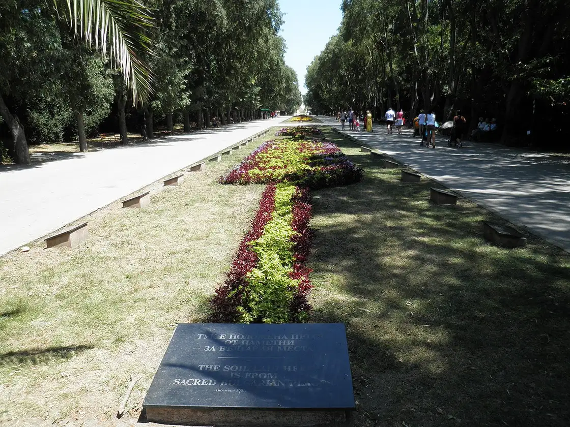 A tree-lined alley with flowerbeds and strolling people in the Sea Garden park in central Varna