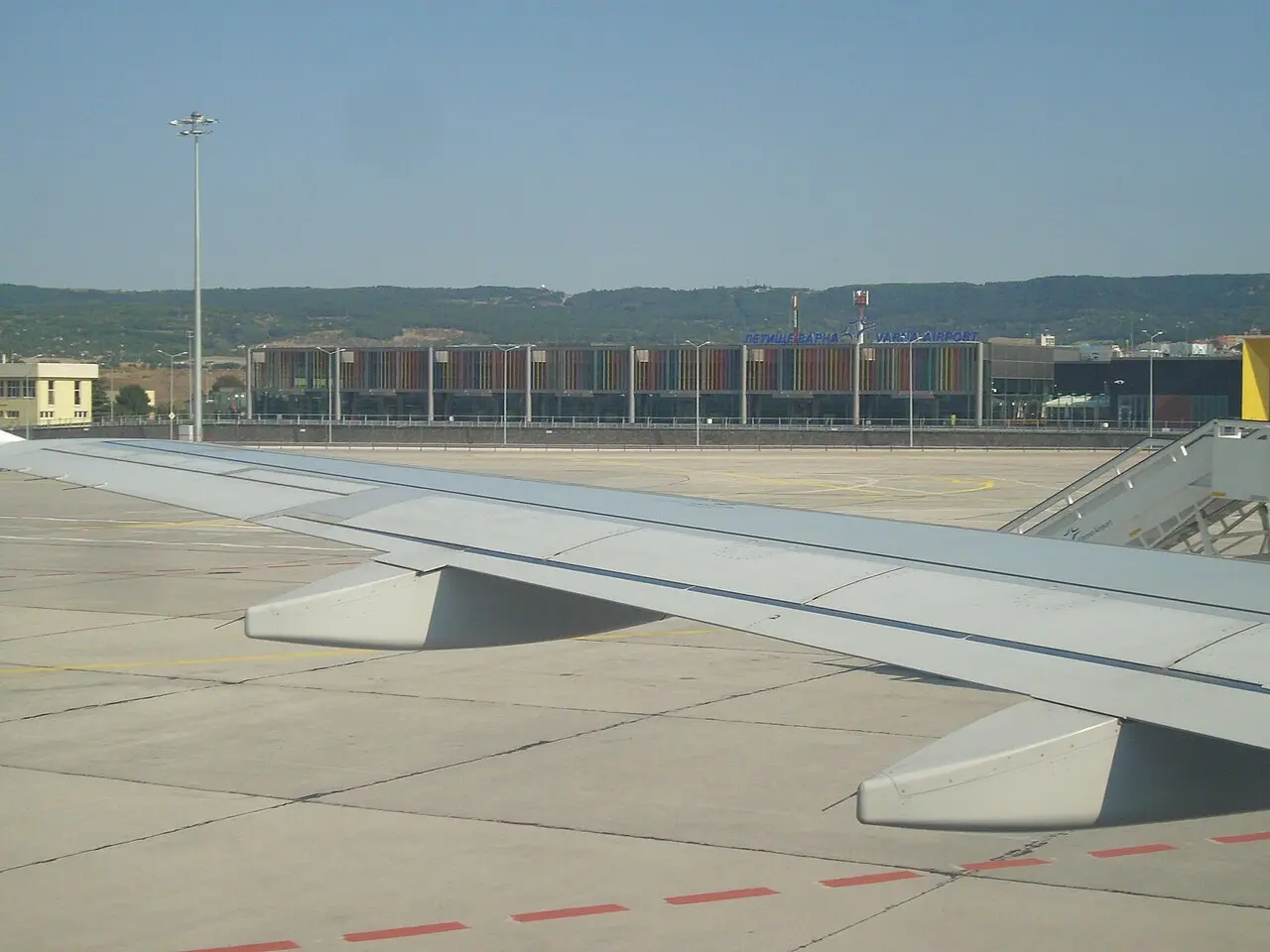 The striped colourful facade of Varna Airport Terminal 2 seen from the apron with an aircraft wing in the foreground