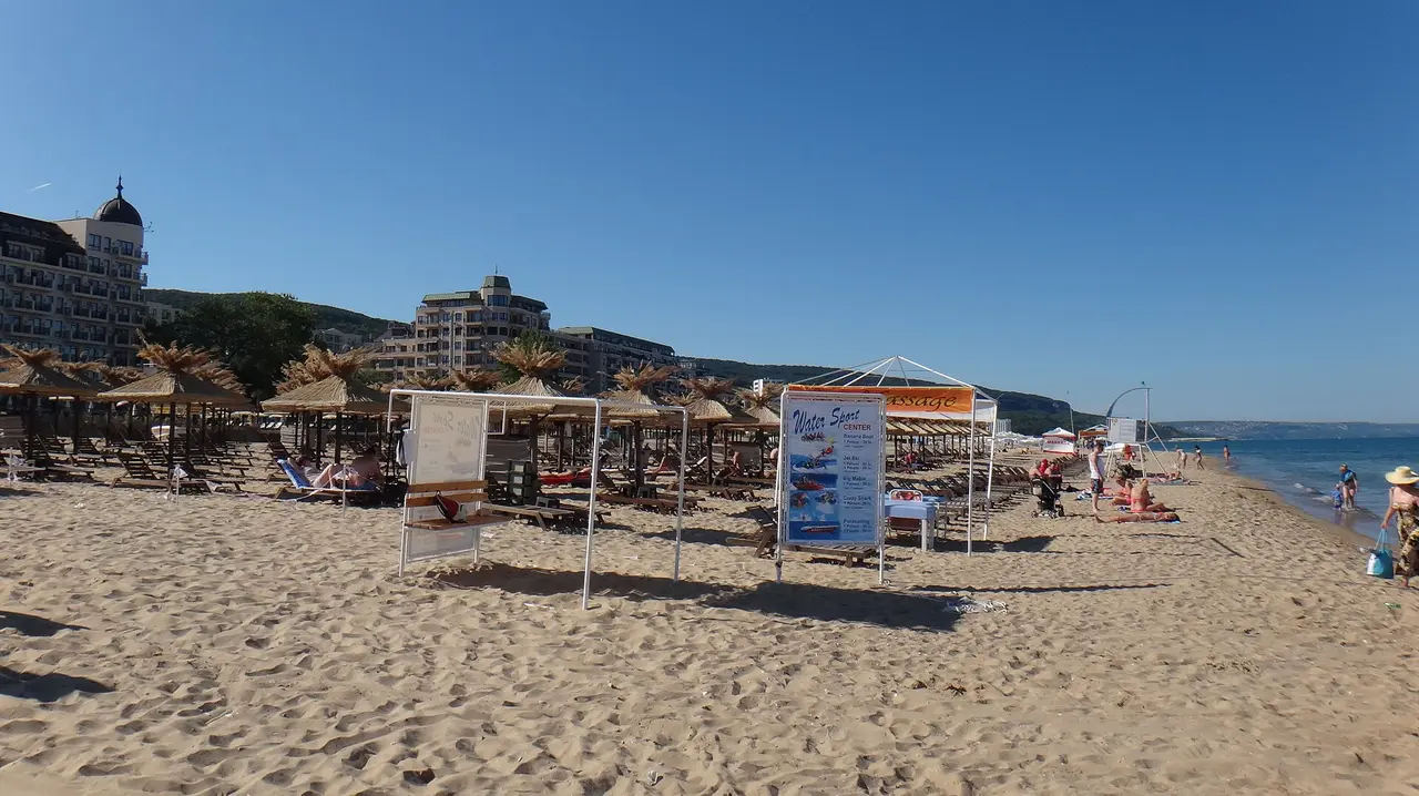The wide sandy beach and hotel strip of Golden Sands seen along the shore with green hills behind