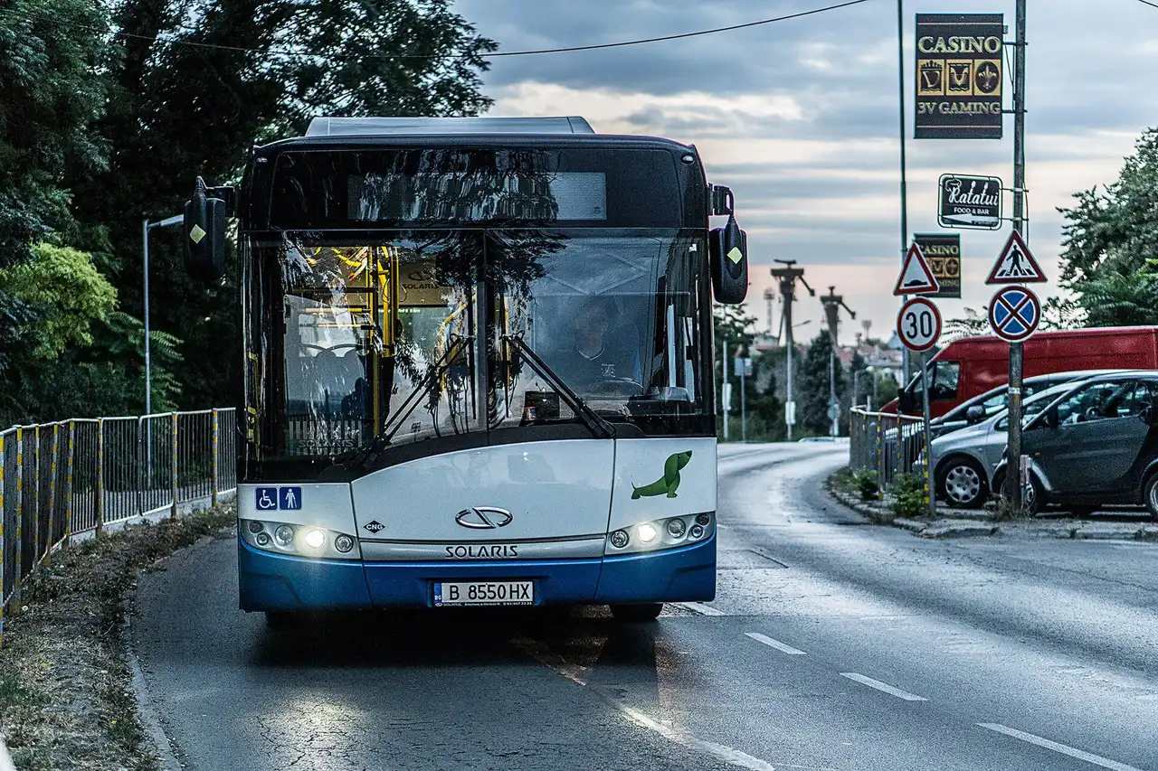 A Varna city bus with headlights on driving the resort road past casino signs at dusk