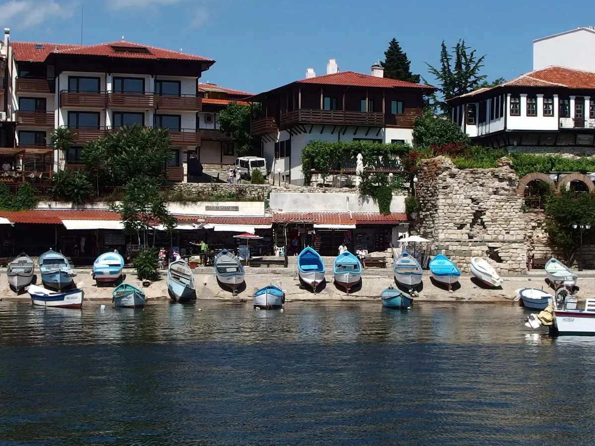 Painted wooden fishing boats drawn up on the stone quay at Nessebar below white houses with dark timber upper storeys and red tiled roofs