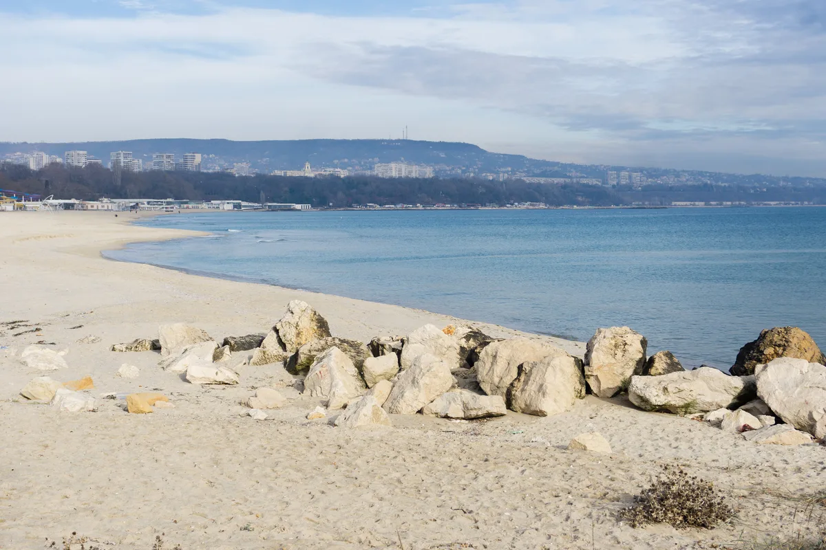 An empty sandy beach in Varna in December, calm blue sea, with the apartment blocks and wooded hills of the city on the horizon