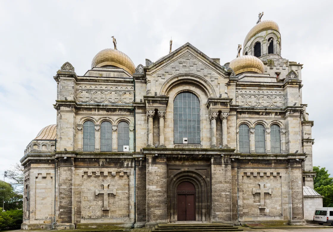 The full stone facade of the Dormition Cathedral in Varna with three gilded onion domes and a large arched central window