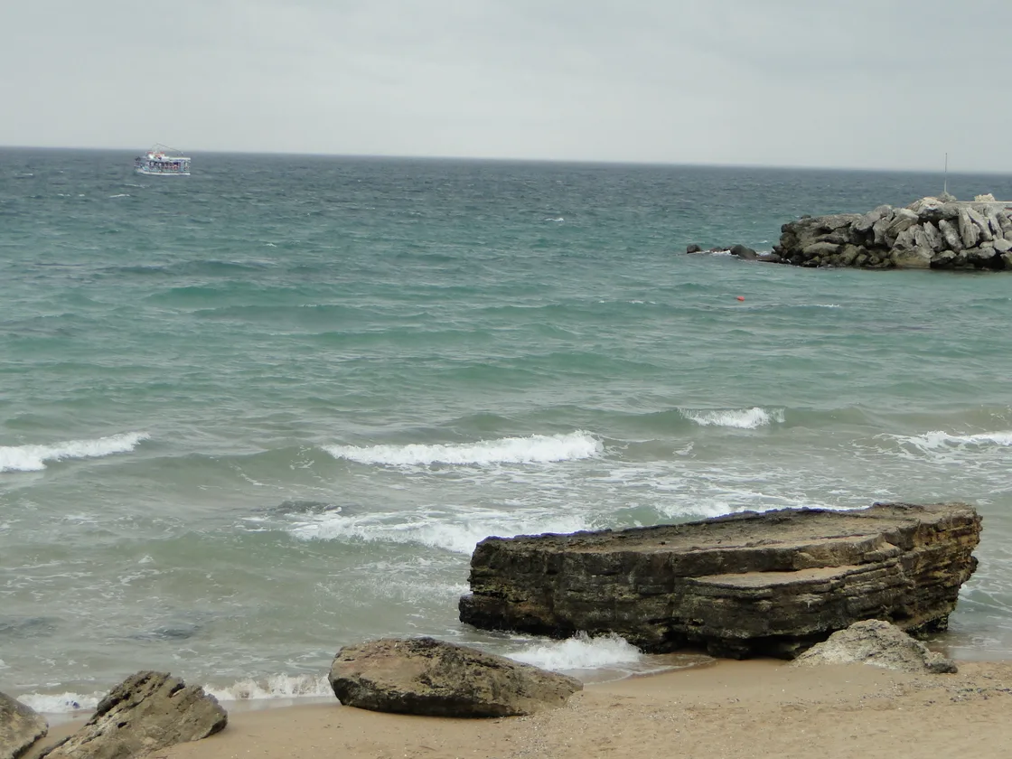 The Black Sea washing onto the shore at Golden Sands resort north of Varna, with a rocky breakwater and a tour boat offshore