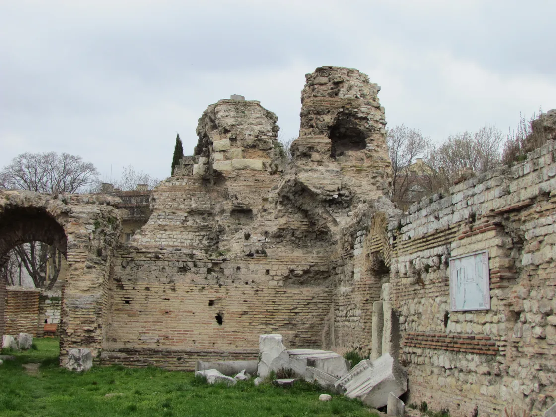 The standing brick-and-stone ruins of the Roman Thermae of Odessos in Varna under a grey sky, with a display board on the wall