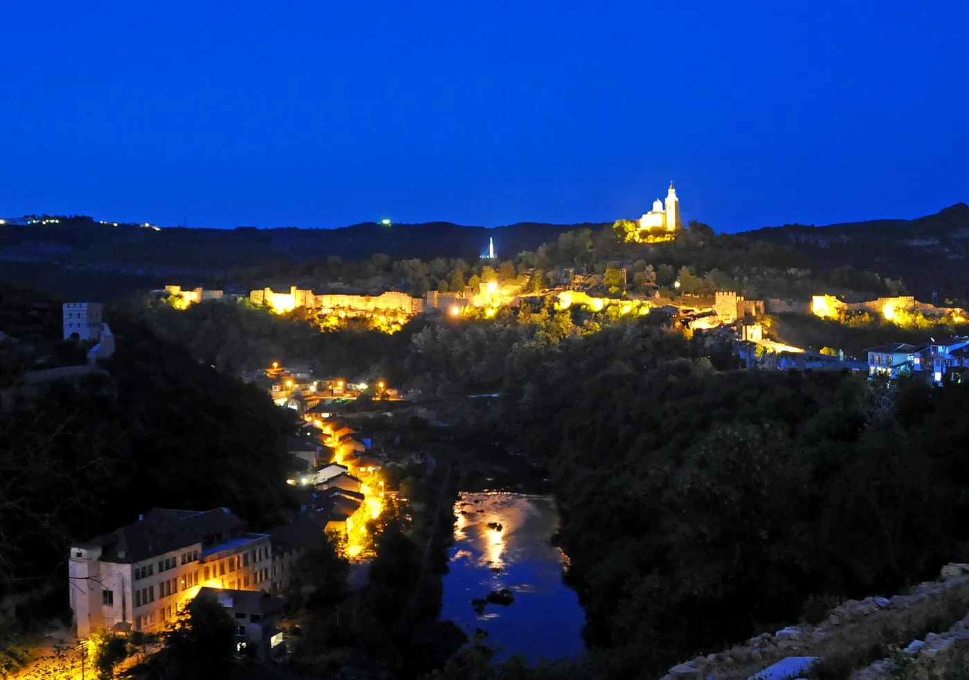 The floodlit walls of Tsarevets fortress and the hilltop cathedral above Veliko Tarnovo at night, with the Yantra river below