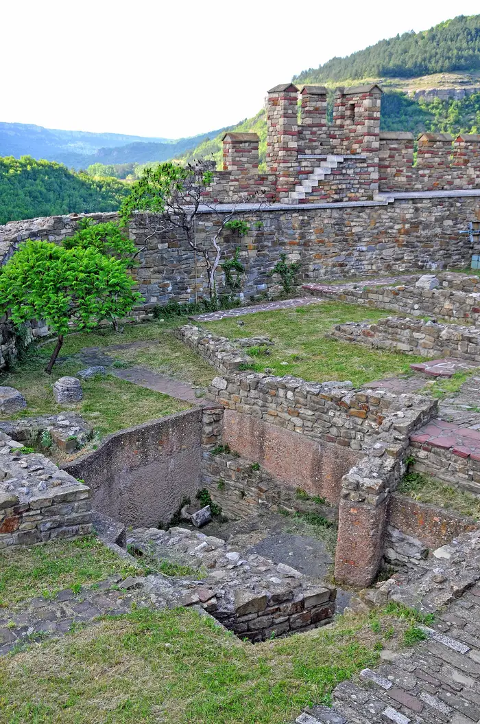 Excavated stone foundations of medieval dwellings inside Tsarevets, backed by a restored battlemented wall