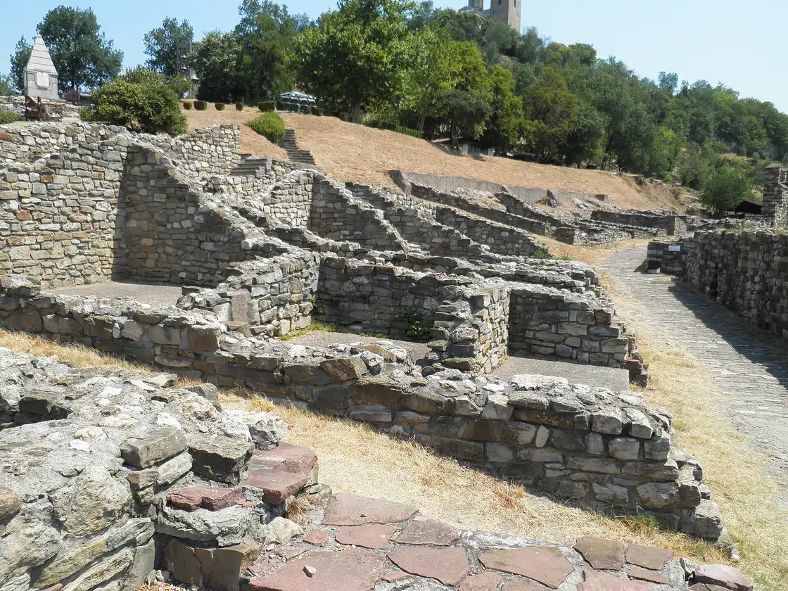 Excavated stone foundations inside Tsarevets fortress with the Patriarchal cathedral tower on the hilltop behind