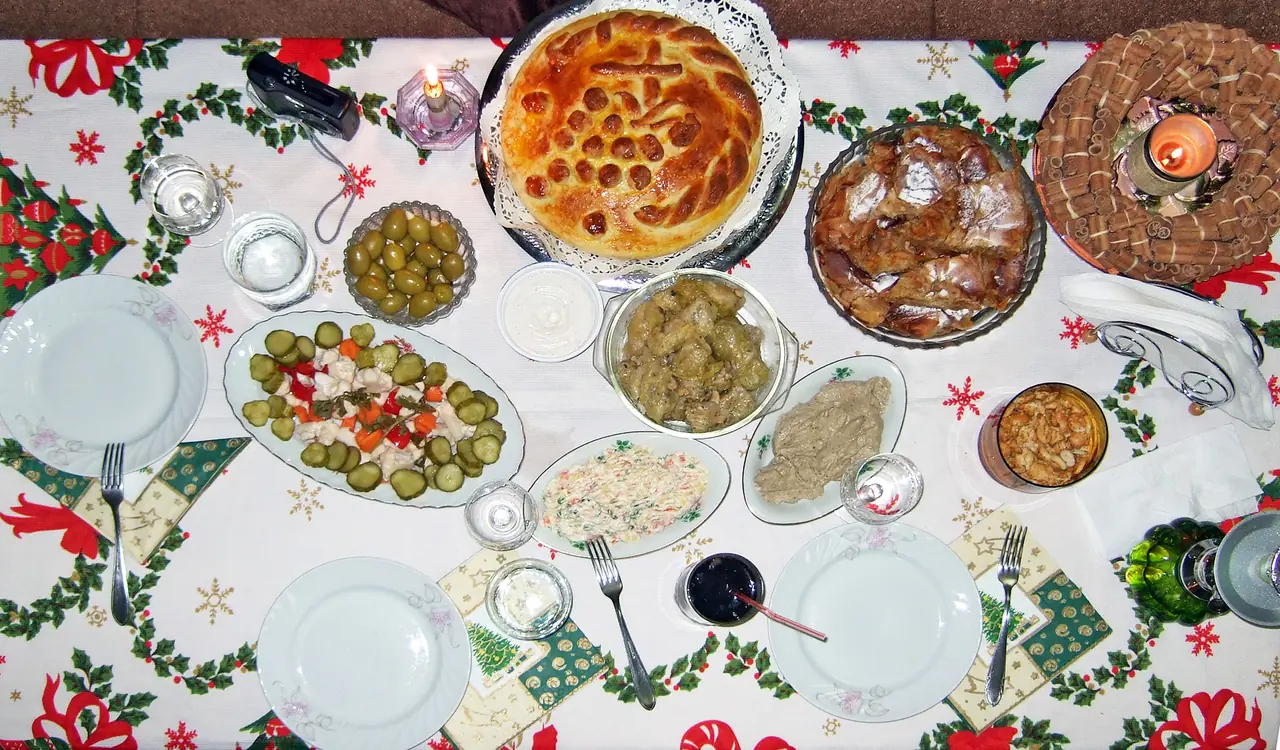 A Bulgarian Christmas Eve table spread with a decorated round loaf, olives, stuffed peppers, sarma, pickle salad and Russian salad on a festive cloth