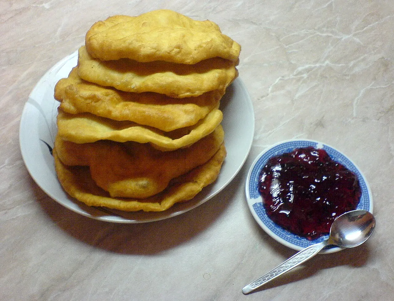 A plate of mekitsi, golden deep-fried dough, served with a dish of dark berry jam