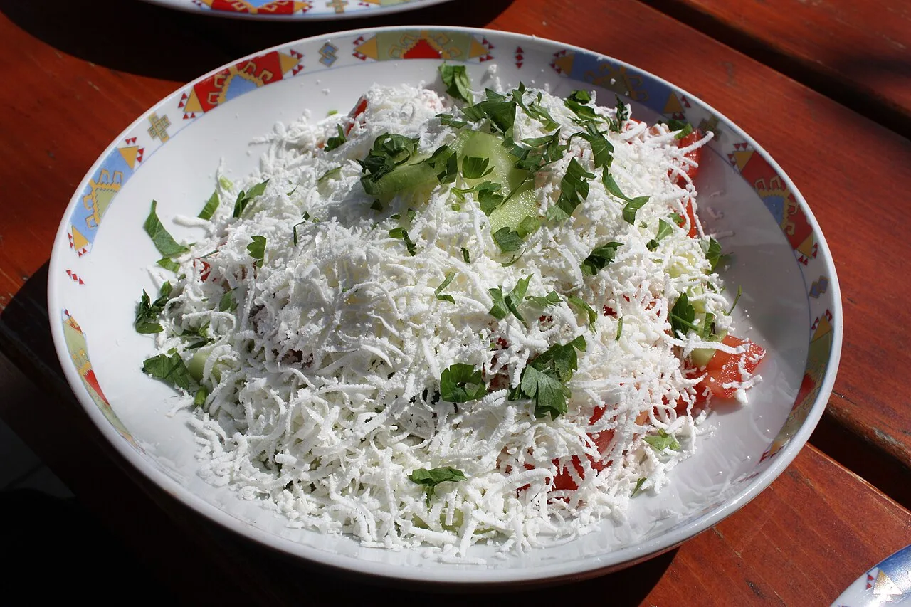 A shopska salad of tomato, cucumber and pepper under a thick layer of grated white sirene cheese, in a Bulgarian folk-pattern bowl