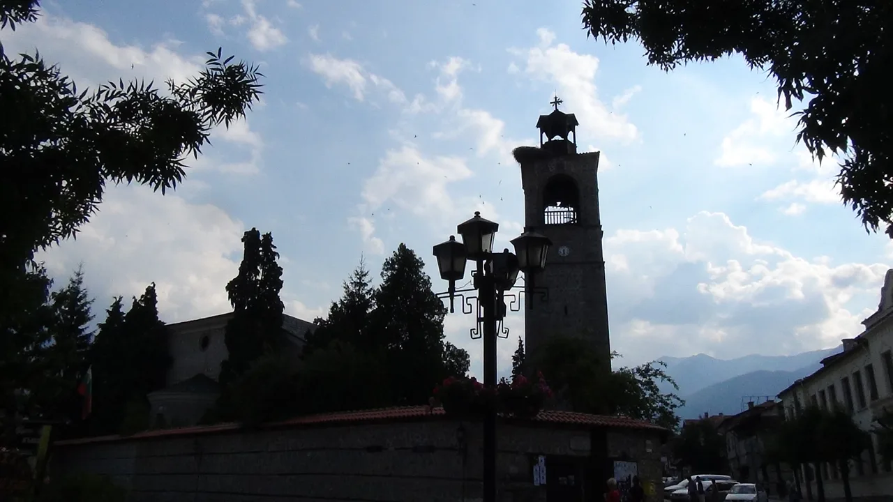 The stone clock tower of Holy Trinity church in Bansko above the street with the Pirin ridge behind