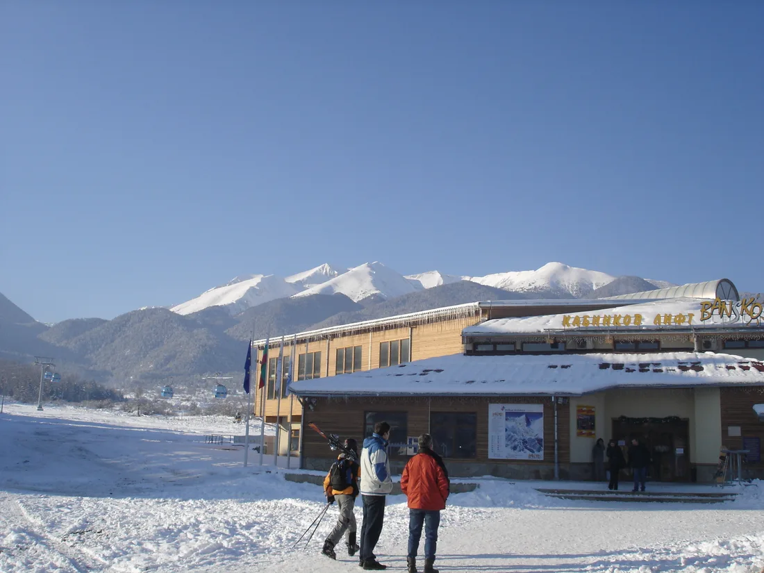 The lower station of the Bansko gondola in winter, with skiers walking across the snow toward the building