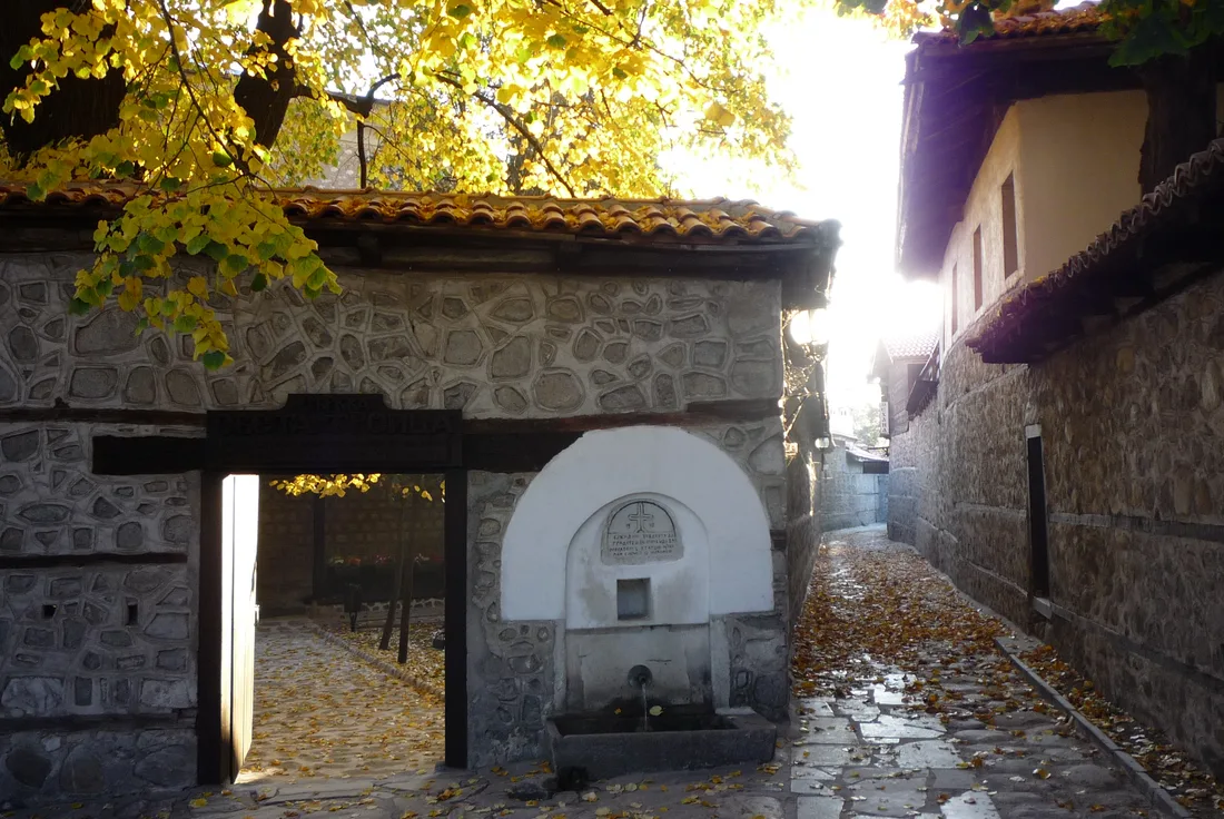 A cobbled lane in the Old Town of Bansko with stone houses, wooden eaves and a covered stone fountain
