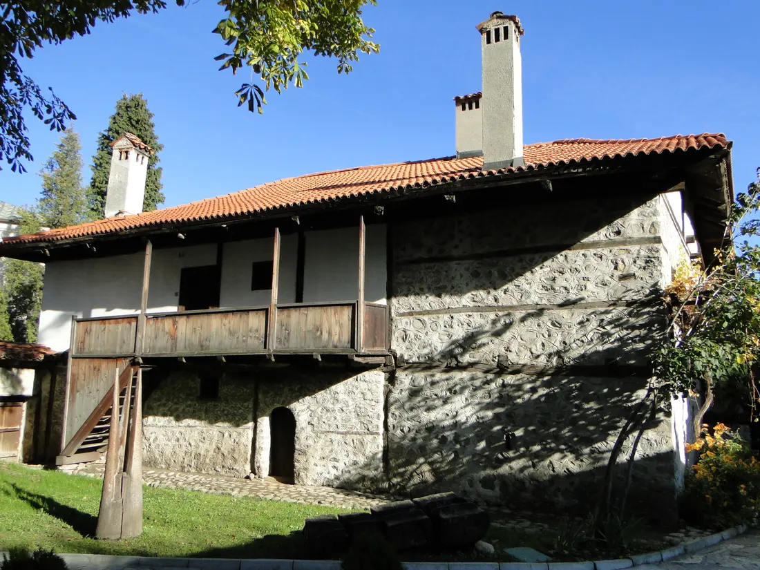 A traditional Bansko Revival house of stone and whitewash with a wooden upper balcony and a red-tiled roof