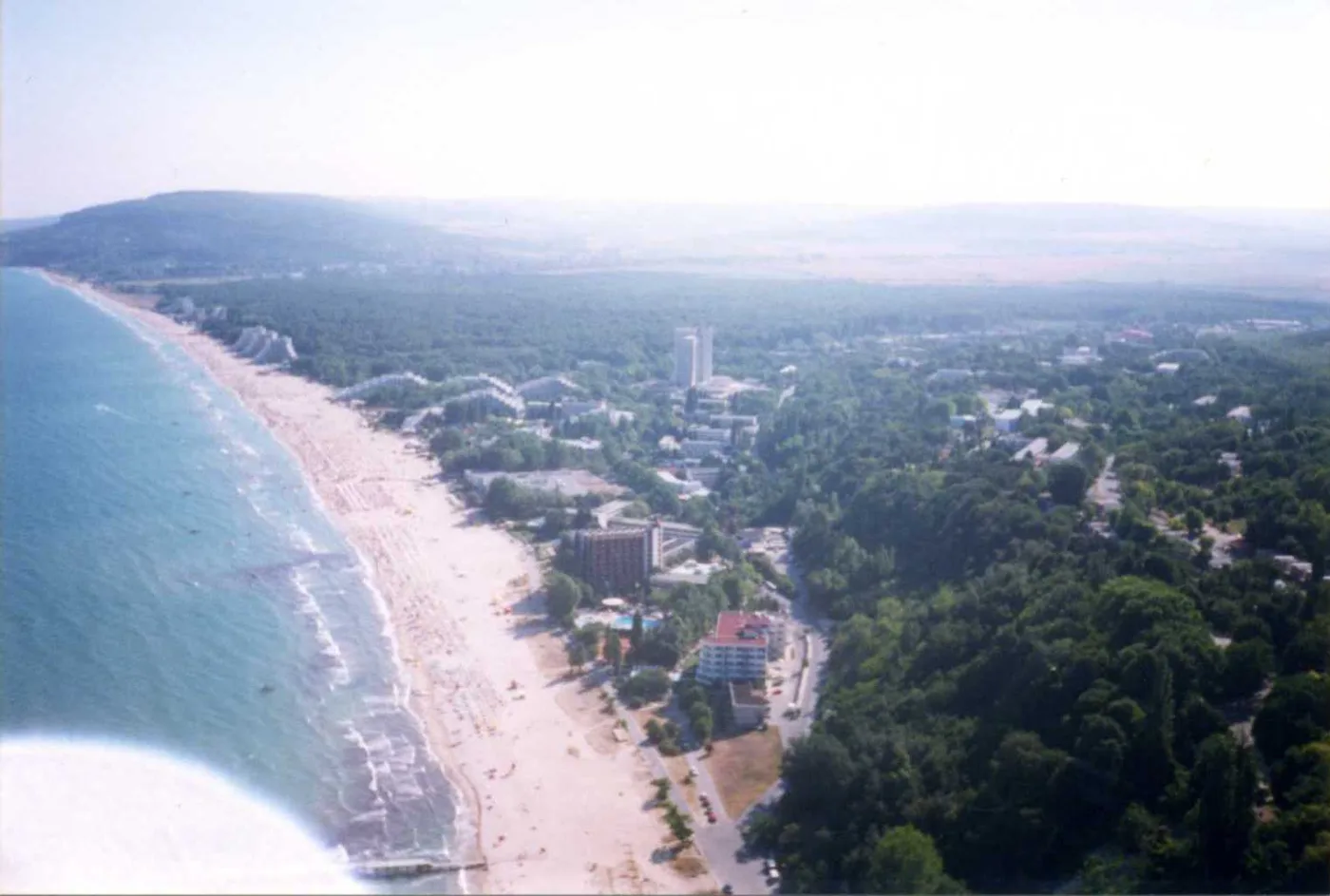 Aerial view of Albena resort, a long curve of sandy beach beside the sea with low-rise hotels set among dense green forest