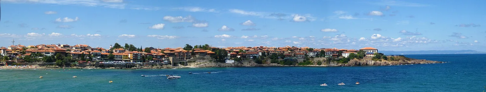 Wide panorama of Sozopol old town on its peninsula, red-roofed houses above turquoise water with small boats in the bay