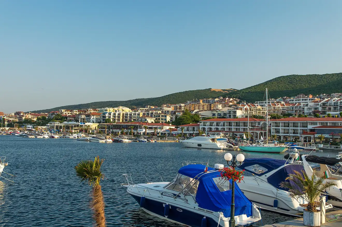 Yachts and motorboats moored at Marina Dinevi in Sveti Vlas at golden hour, low resort buildings and green hills behind