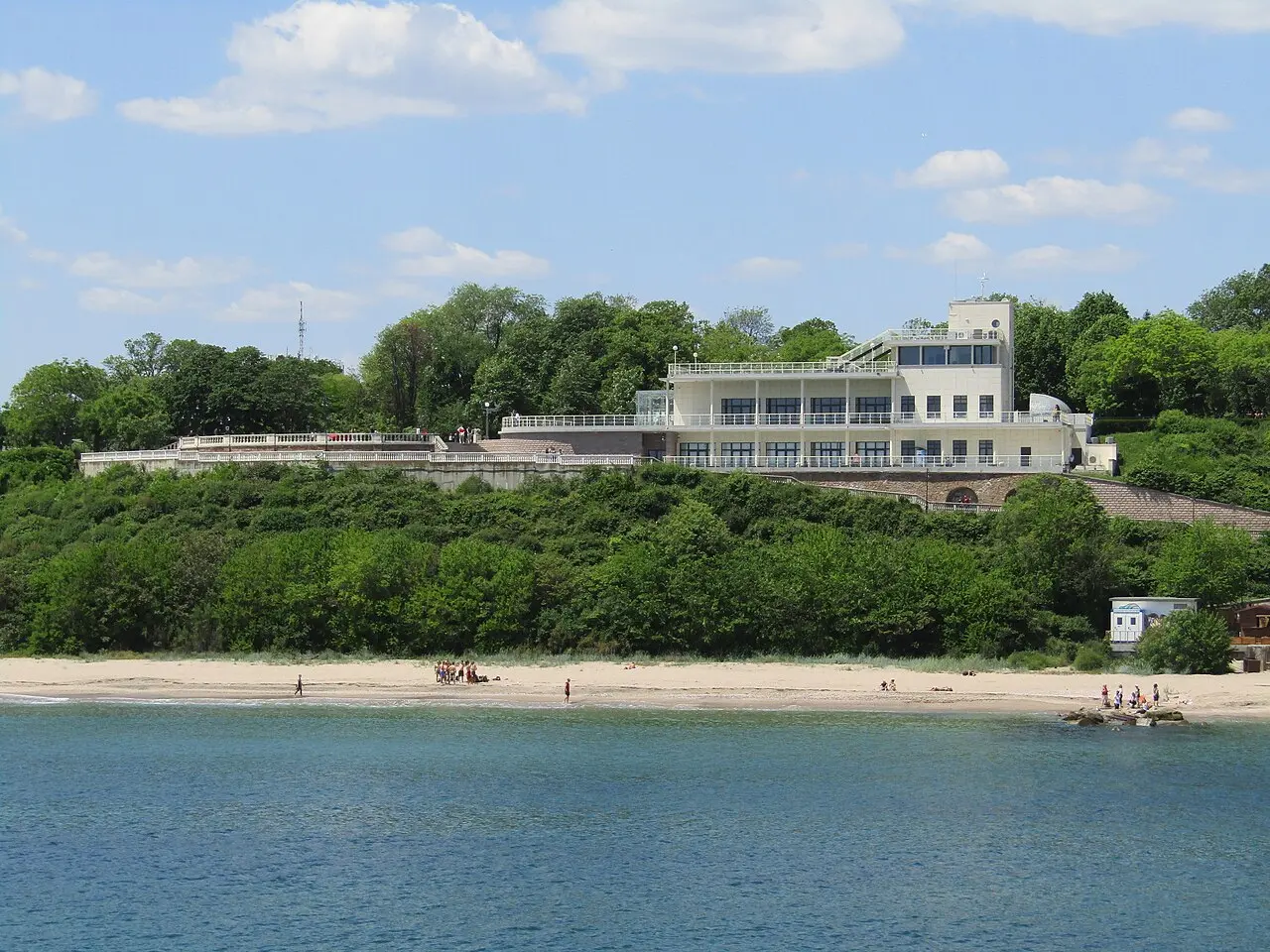 The white Marine Casino building in Burgas Sea Garden with its curved facade and people walking on the paths around it