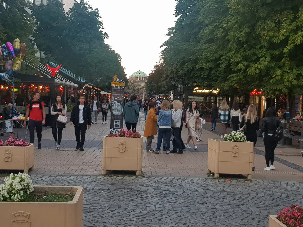 The pedestrianised Vitosha Boulevard in Sofia at dusk, lined with cafes and trees, with the dome of St Nedelya Church at the far end