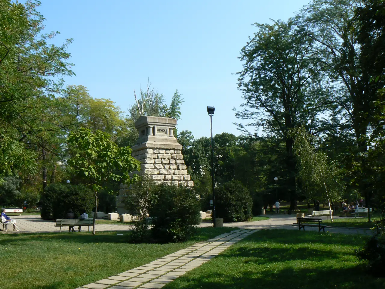 The Doctor's Garden park in Oborishte, Sofia, a shady green space with a stone monument, benches and trees