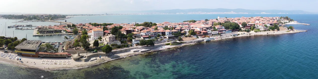 Wide panorama of the Nessebar peninsula covered in red-roofed houses, joined to the mainland by a narrow isthmus