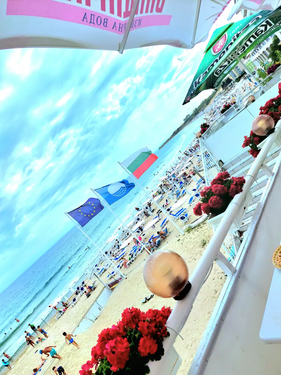 South Beach in Nessebar seen from a balcony, with rows of umbrellas, sunbeds and swimmers in the shallow water