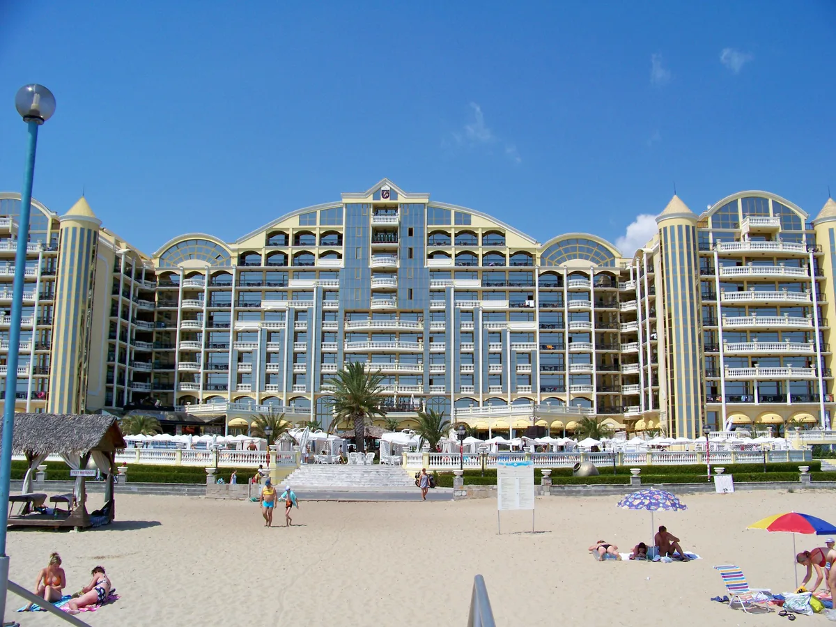 A large beachfront resort hotel in Sunny Beach with balconies and palm trees, seen from the sand