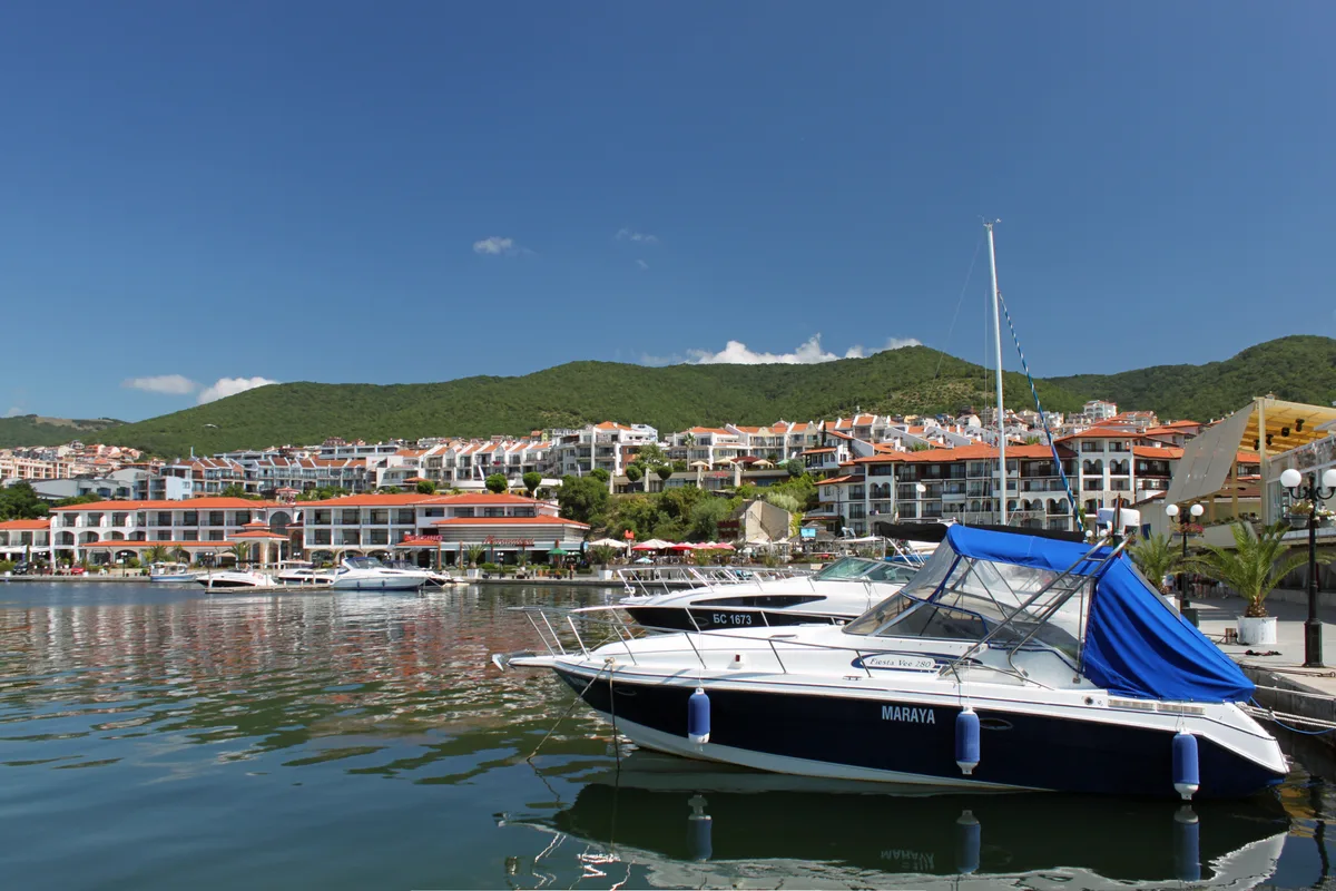 Sveti Vlas seen from the water, with apartment blocks on wooded slopes above the marina and yachts moored below