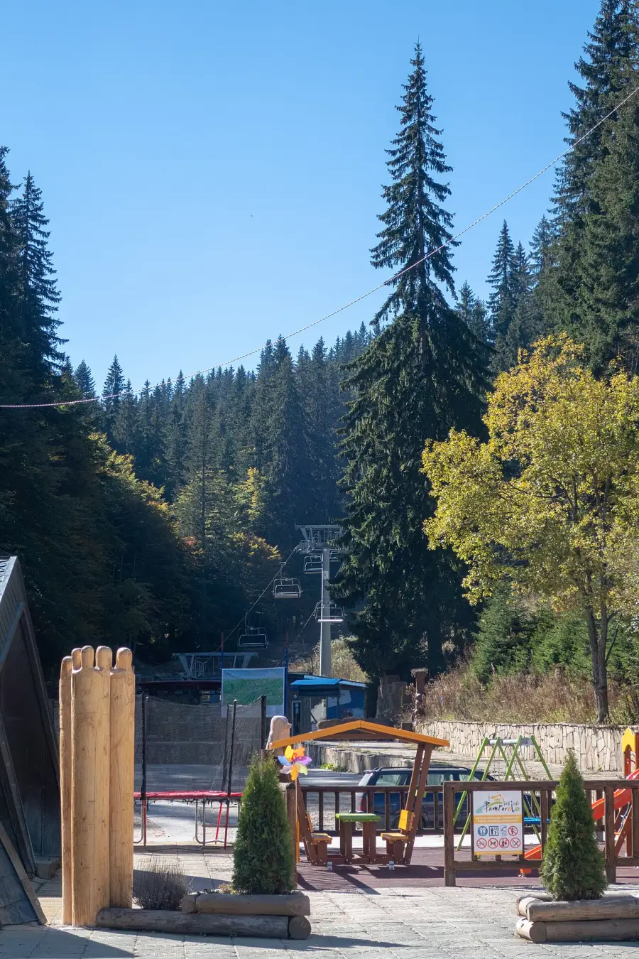 A chairlift base at Pamporovo with a children's play area beside it among tall pines in autumn