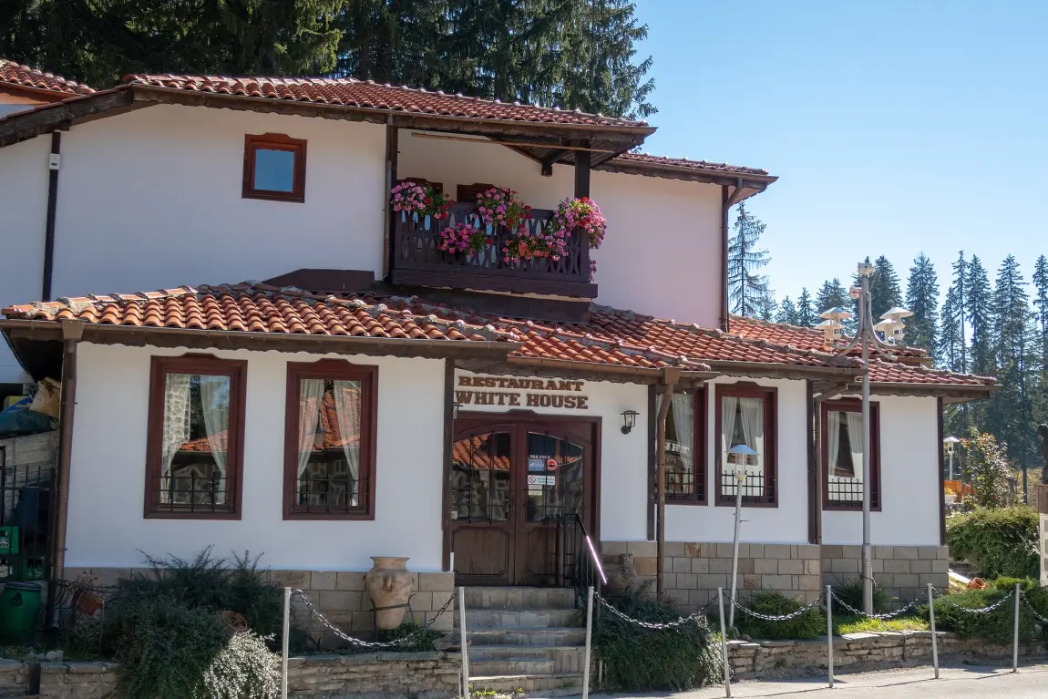 A traditional Rhodope-style restaurant building called White House with stone walls, timber balcony and red-tiled roof at Pamporovo