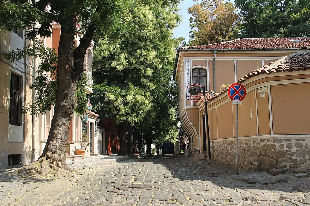 A cobbled lane in the Old Town of Plovdiv with an ochre National Revival house and a large tree
