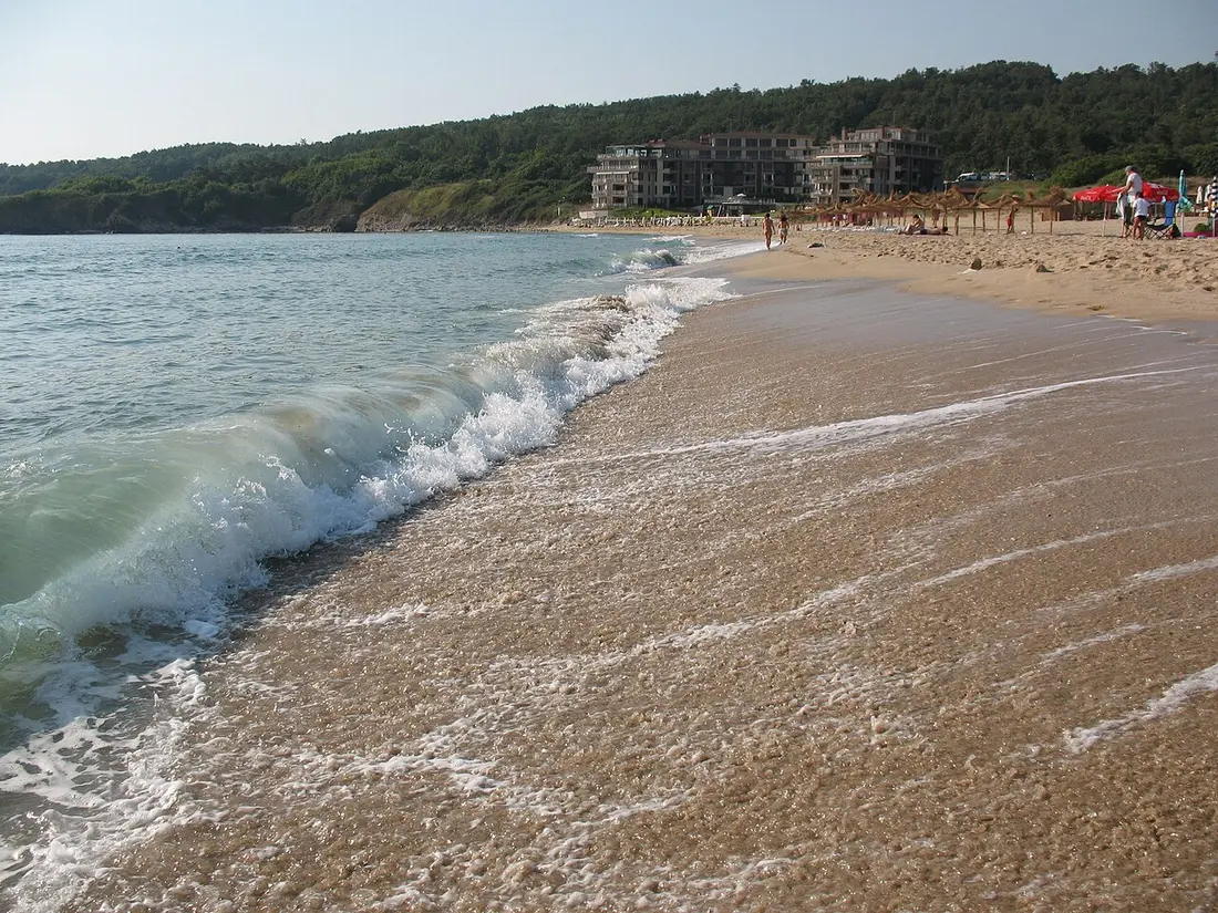 Kavatsi beach south of Sozopol, waves breaking on wide sand with apartment complexes on the forested slope behind