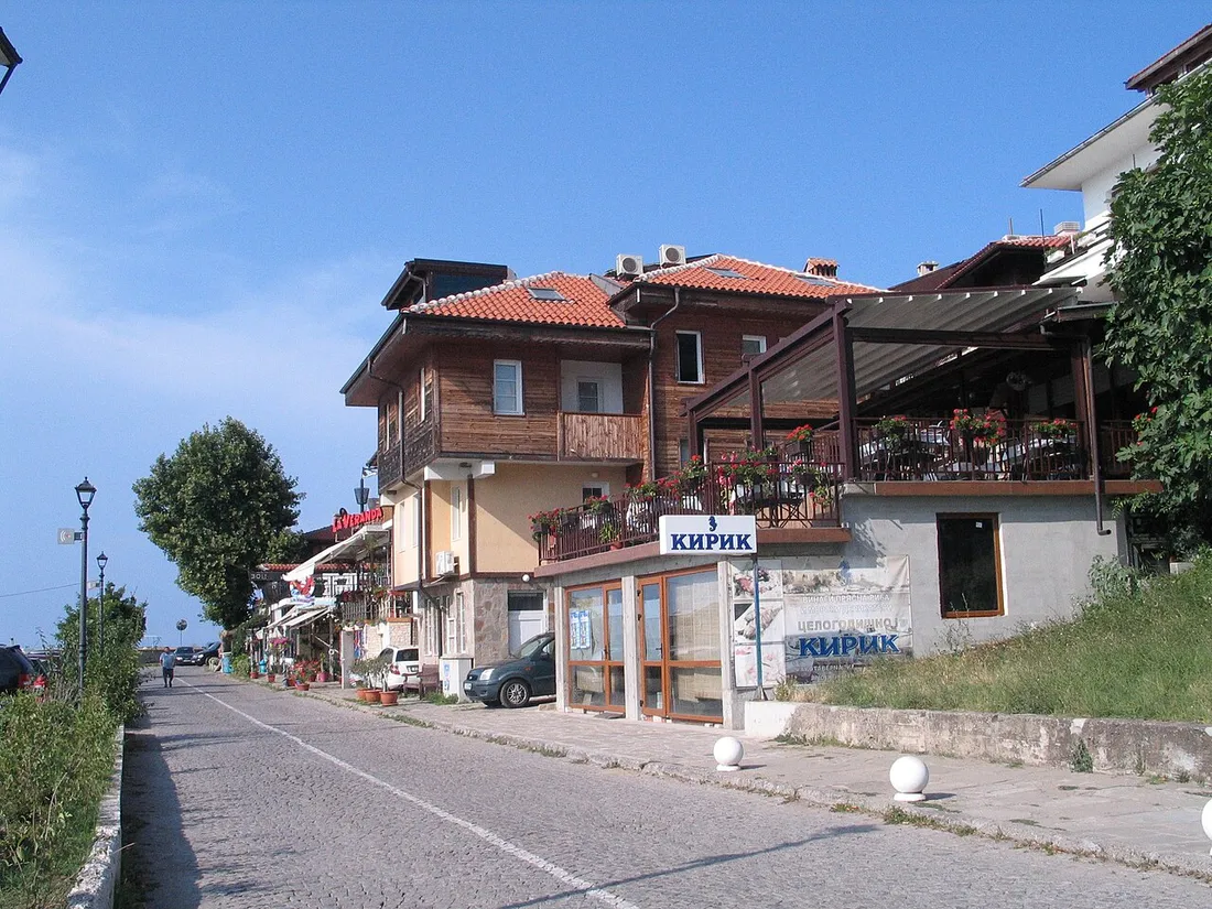A cobbled lane in Sozopol old town with a timber-clad Revival house, a shop terrace and a car parked at the edge of the pedestrian zone