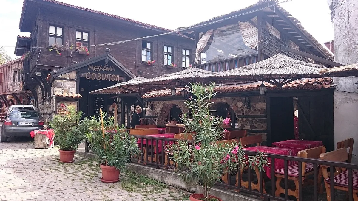 A timber Revival house turned tavern in Sozopol old town, with a thatched terrace, red tablecloths and oleander pots on a cobbled street