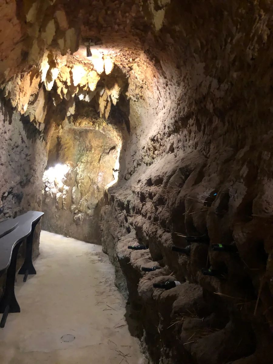 A rock-cut wine cellar tunnel in Melnik with rough sandstone walls and a wooden table along one side