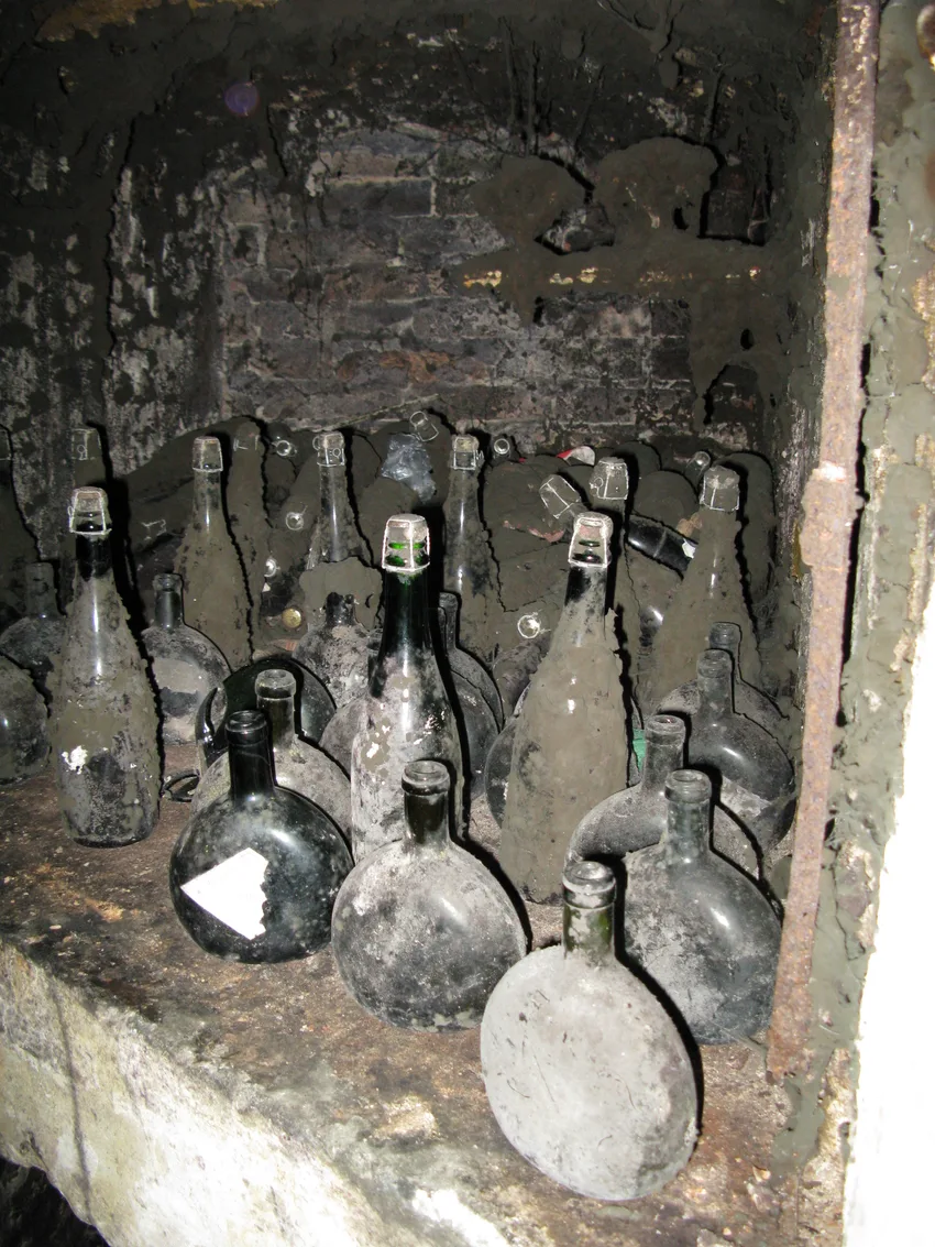 Old dusty glass demijohns and bottles standing in a niche cut into a rock wall in Melnik