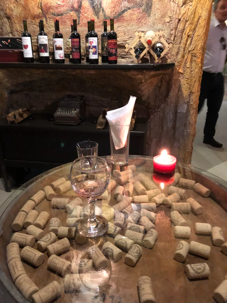 A tasting set-up on a barrel head in a Melnik cellar with a wine glass, candle, scattered corks and bottles on a rock shelf behind